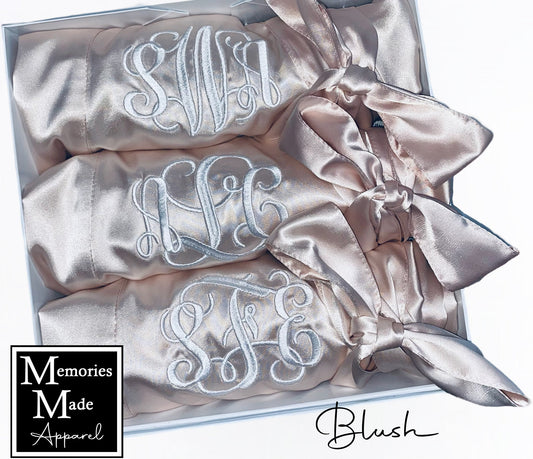 Three blush robes with custom embroidered monograms on the left chest.  Each robe is rolled and tied with the robes satin belt. The robes are displayed in a white box against a white background. The logo for Memories Made Apparel is in the lower left corner. The word blush is in the lower right hand corner. 