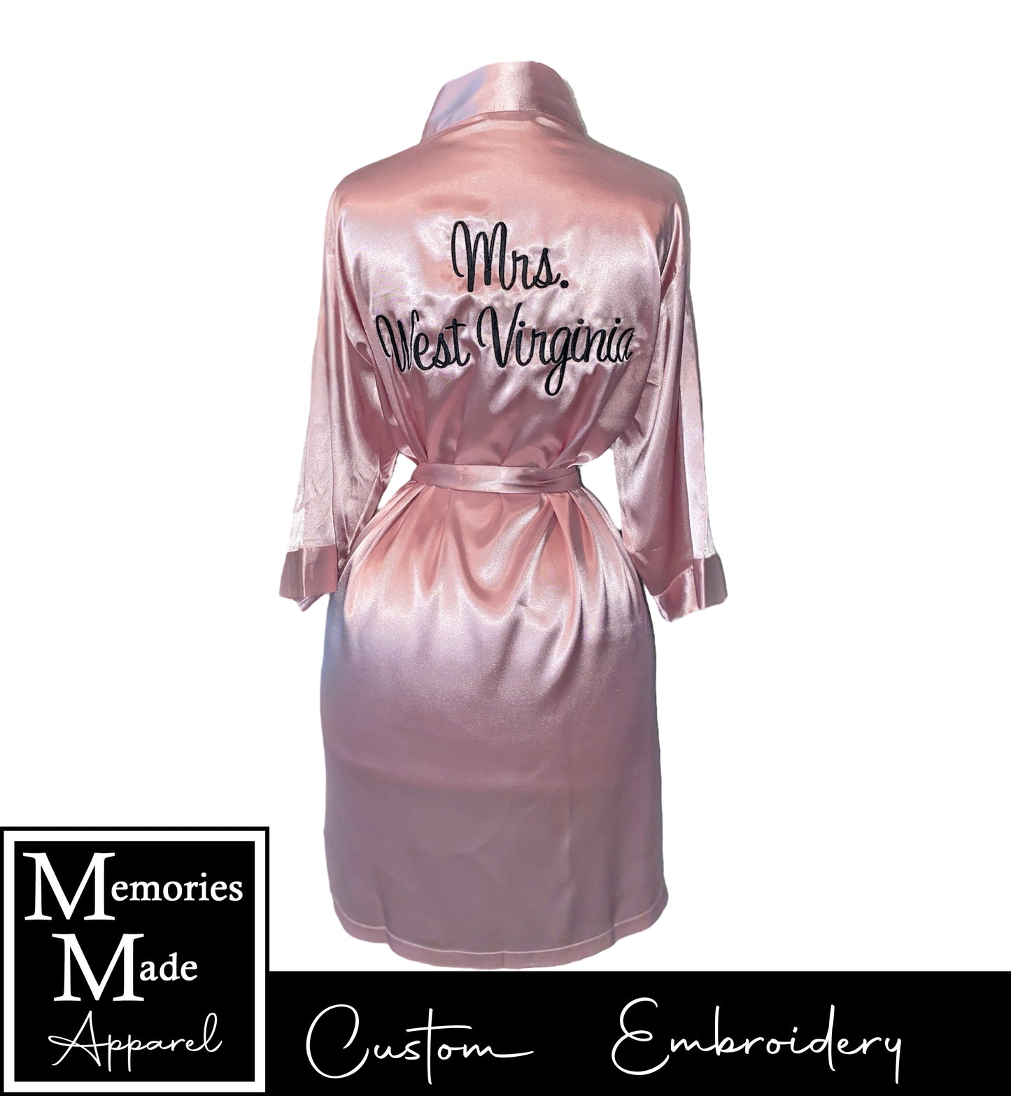 Pink robe on a mannequin with custom embroidery across the back in black thread. on the left chest. The robe is displayed against a white background. The logo for Memories Made Apparel is in the lower left corner. 
